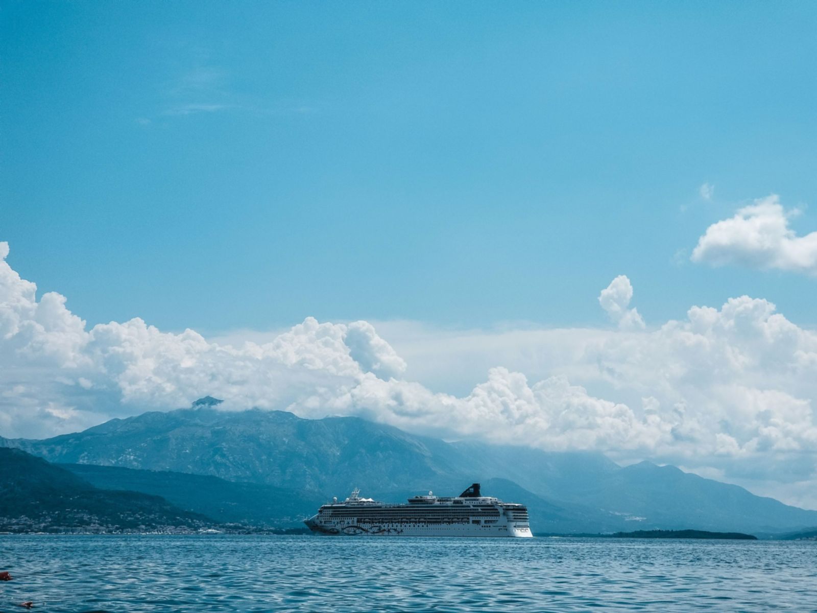 Cruise ship sailing in calm water below misty green mountains