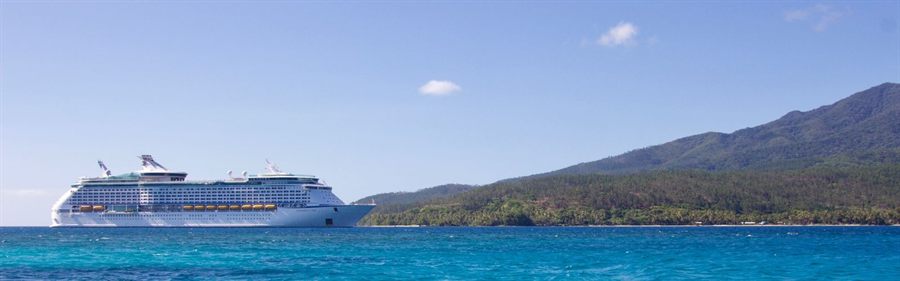 Cruise ship at sea off a green tropical island under a blue sky