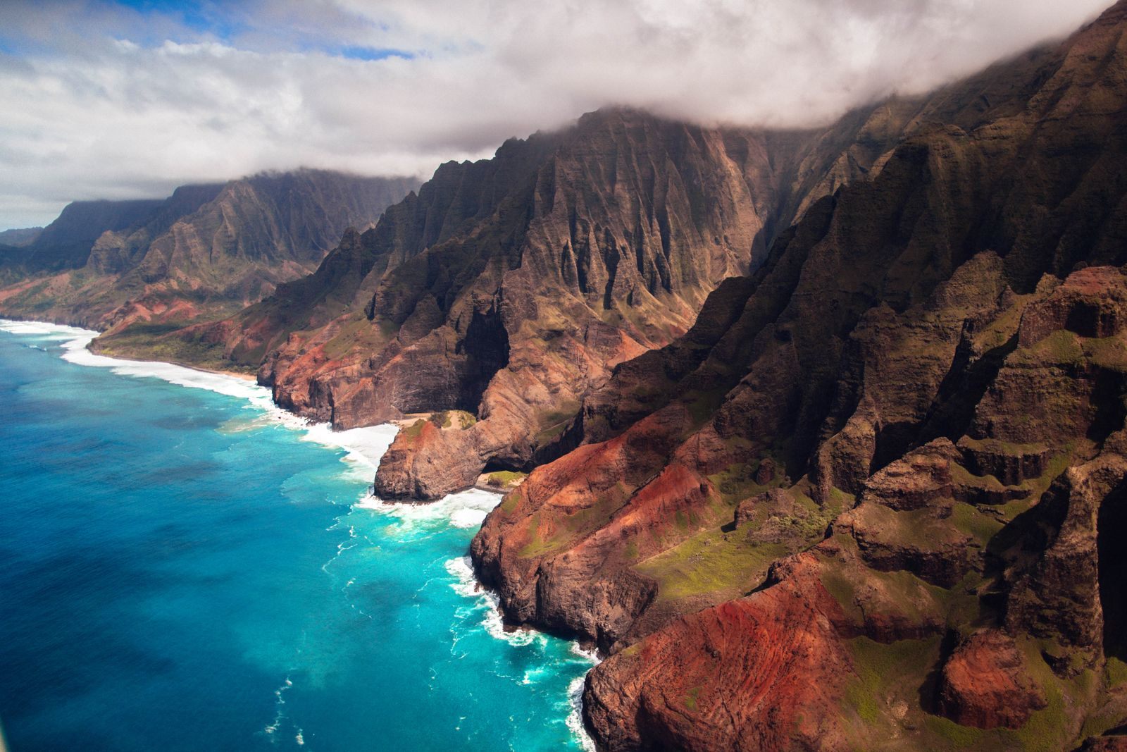 Aerial view of the Na Pali Coast on Kauai, a highlight of Hawaiian cruises, with sheer green ridges above turquoise surf