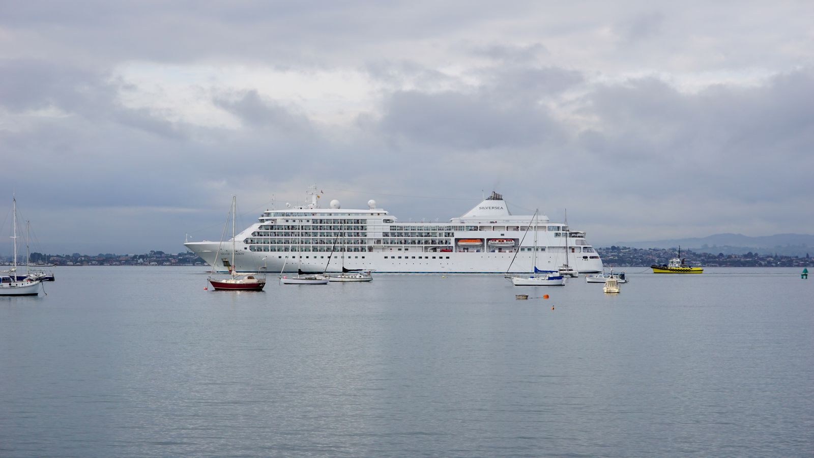 Small white luxury cruise ship at anchor among local boats in a calm bay